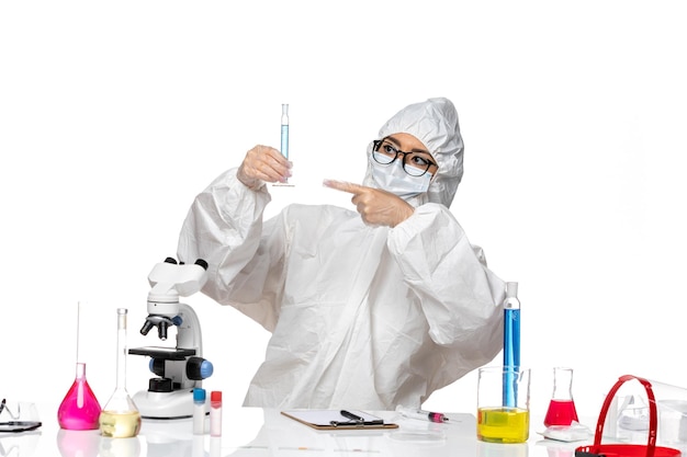 正面図白い背景の実験室covid化学ウイルスに青い溶液とフラスコを保持している特別な防護服の若い女性の化学者