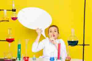 Foto gratuita chimico femminile giovane vista frontale che si siede in vestito bianco con diverse soluzioni che tengono segno bianco sul processo di scienza chimica pavimento giallo