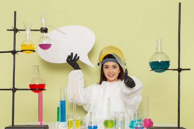 녹색 벽 화학 실험실 화학 직업 여성 과학에 큰 흰색 기호를 들고 특수 보호 복에 전면보기 젊은 여성 화학자