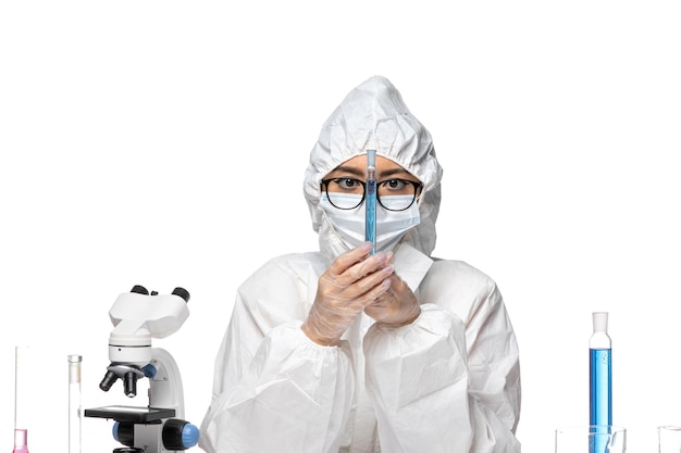 Front view young female chemist in special protective suit holding flask with blue solution on a light white background covid- chemistry virus lab