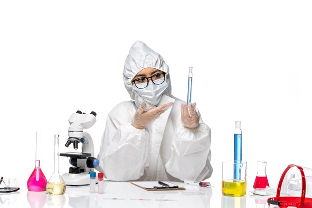 正面図明るい白の背景に青い溶液とフラスコを保持している特別な防護服の若い女性化学者covid化学ウイルスラボ