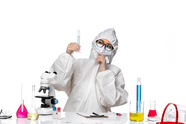 Вид спереди молодая женщина-химик в специальном защитном костюме, держащая колбу с синим раствором на светлом белом фоне, лабораторный вирус химии ковид