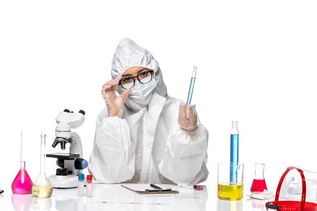 Front view young female chemist in special protective suit holding flask with blue solution on white background covid chemistry virus lab