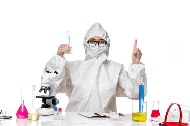 Front view young female chemist in special protective suit holding flask with blue solution on a white background lab covid chemistry virus