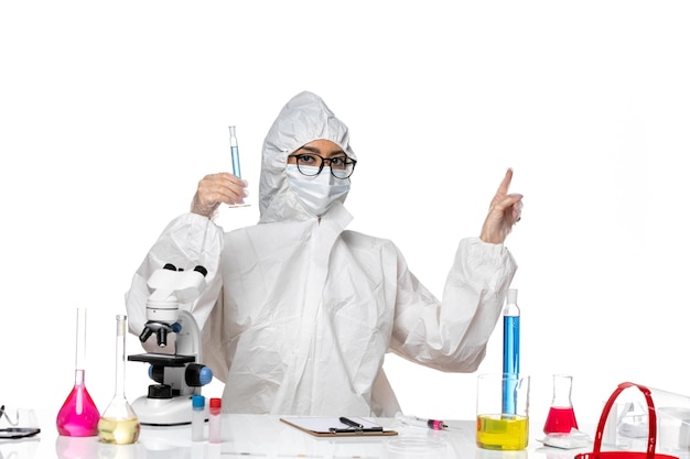 Front view young female chemist in special protective suit holding flask with blue solution on the white background lab covid chemistry virus