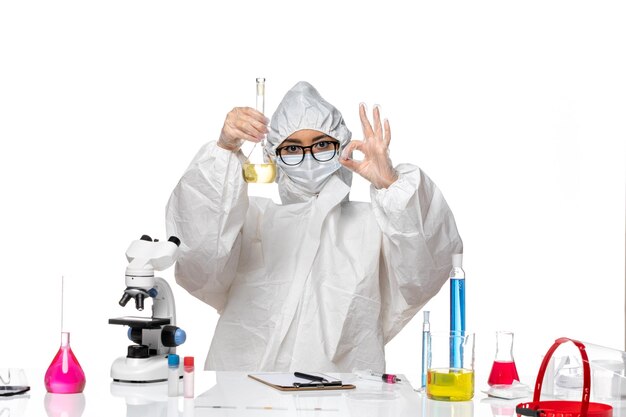 Вид спереди молодая женщина-химик в специальном защитном костюме, держащая колбу с раствором на белом фоне, лабораторный вирус химии ковид