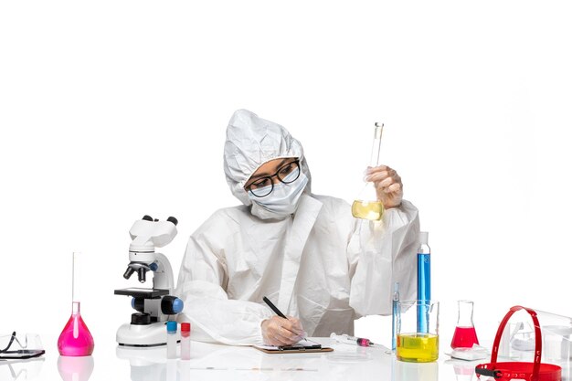 Front view young female chemist in special protective suit holding flask with solution on a white background lab covid virus chemistry