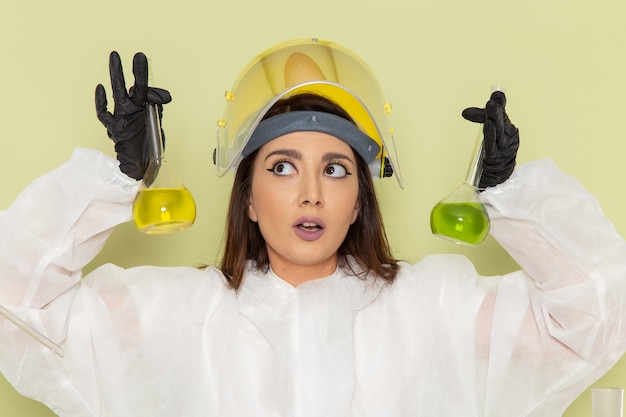 Chimico femminile giovane vista frontale in vestito protettivo speciale che tiene boccette con soluzioni sul laboratorio di scienze femminili di lavoro chimica chimica scrivania verde