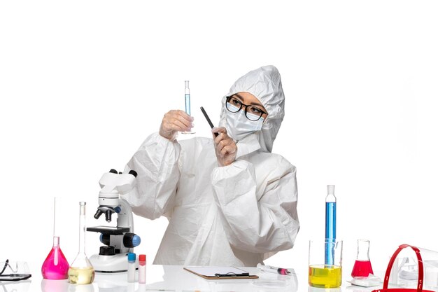 Front view young female chemist in special protective suit holding tiny flask on a white background lab covid chemistry virus