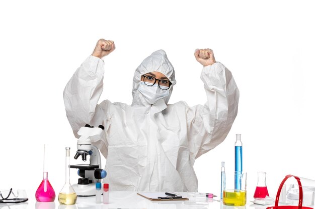 白い机の上に座って喜んでいる特別な防護服を着た若い女性化学者の正面図ウイルスラボcovid化学