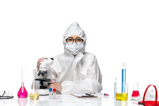 흰색 책상 바이러스 실험실 COVID 건강 화학에 현미경을 사용하여 특수 보호 복에 전면보기 젊은 여성 화학자
