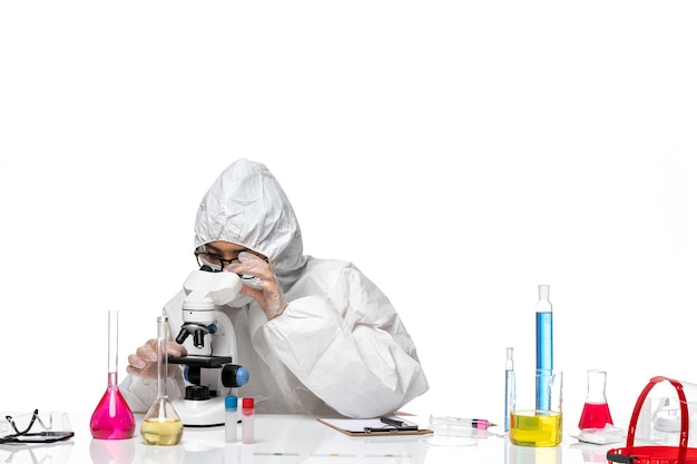 Front view young female chemist in special protective suit working with microscope on the light white background covid- chemistry lab virus