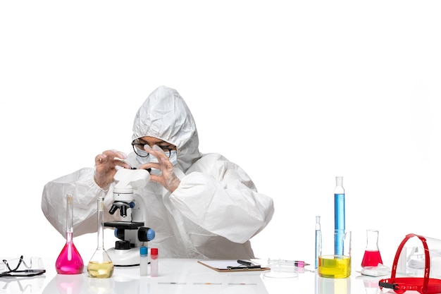 Вид спереди молодая женщина-химик в специальном защитном костюме, работающая с микроскопом на белом фоне, вирусная химическая лаборатория covid