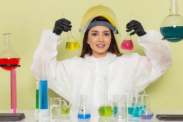 Вид спереди молодая женщина-химик в специальном защитном костюме, работающая с растворами на зеленом столе, химическая химия, женская научная лаборатория