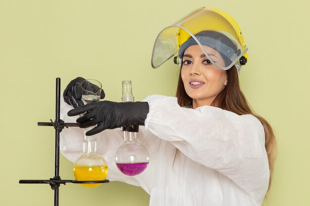 Front view young female chemist in special protective suit working with solutions on green wall chemical lab chemistry job female science