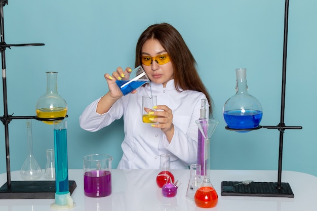 Free photo front view of young female chemist in white suit in front of table working with colorful solutions