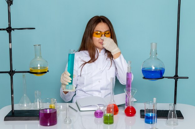 Вид спереди молодой женщины химик в белом костюме перед столом, работающих с решениями