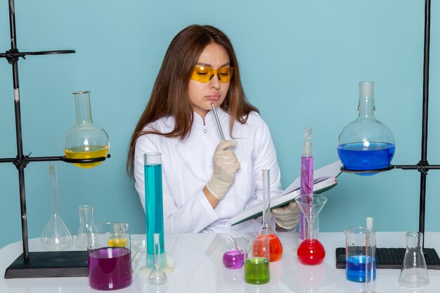 Front view of young female chemist in white suit in front of table working with solutions