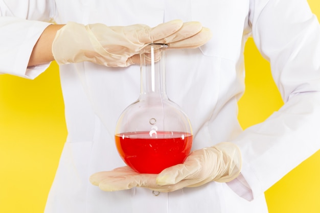 Front view of young female chemist in white suit holding chemical solution