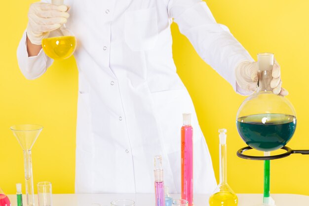 Front view of young female chemist in white suit holding chemical solutions working with them