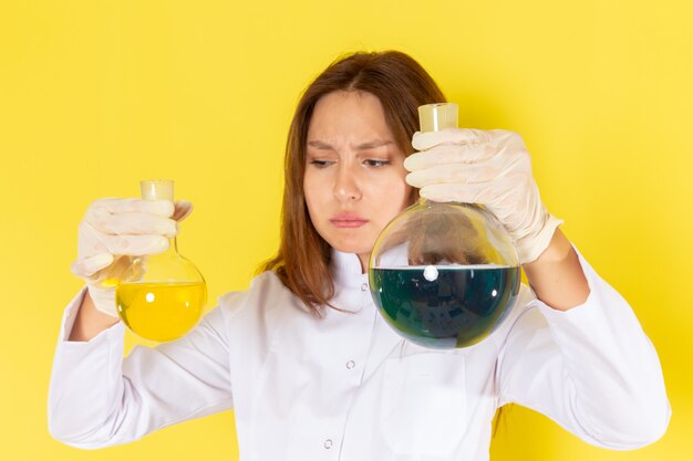 Front view of young female chemist in white suit holding chemical solutions