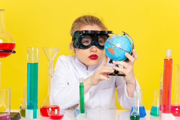 Вид спереди молодая женщина-химик в белом костюме с решениями ed проверяет глобус с маской на желтом космическом химическом науке