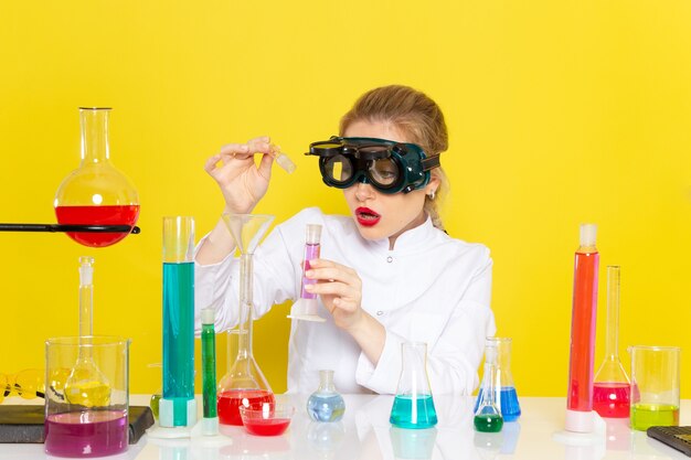 Front view young female chemist in white suit with ed solutions working with them and sitting on the yellow space chemistry 