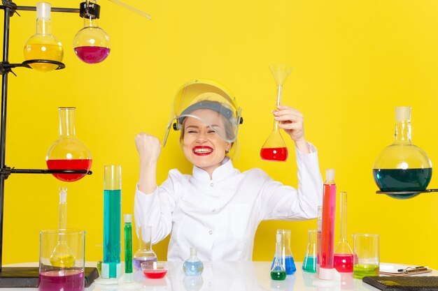 Free photo front view young female chemist in white suit with ed solutions working with them wearing helmet with joy on the yellow space chemistry science s