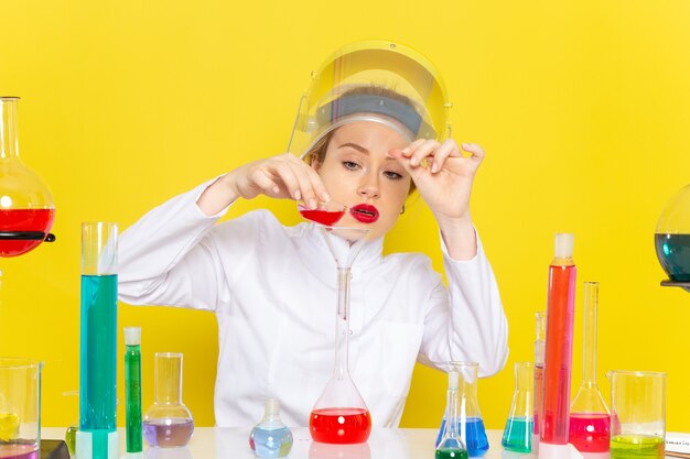 Front view young female chemist in white suit with ed solutions working with them wearing helmet on the yellow space chemistry science s process job