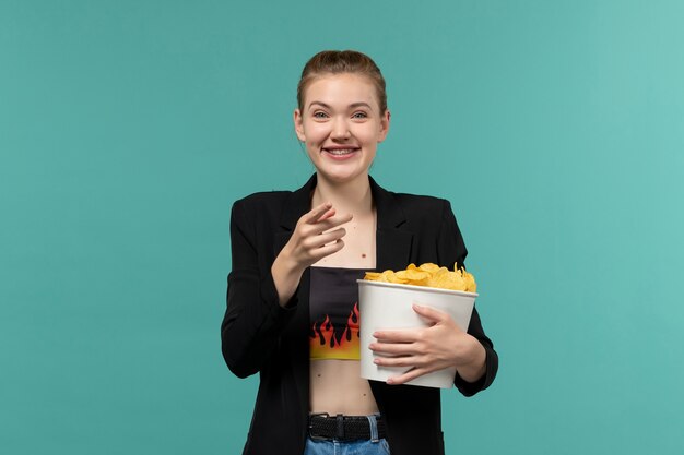 Front view young female in cinema eating potato chips watching movie on blue surface