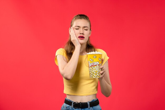 Front view young female at cinema holding popcorn and having toothache on red wall movie theater cinema snack female fun film