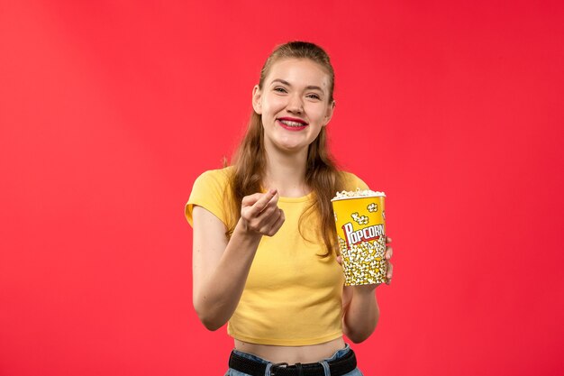 Front view young female at cinema holding popcorn and laughing on the red wall movie theater cinema female fun film