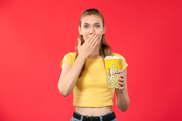 明るい赤の壁にポップコーンを保持している映画館で若い女性の正面図映画館の女性の色