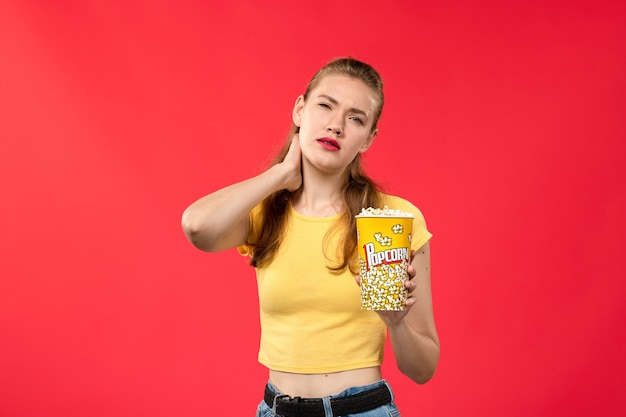 Вид спереди молодая женщина в кино, держащая пакет попкорна и имеющая шейную боль на красной стене кинотеатр кинотеатр женский забавный фильм