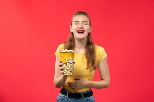 Front view young female at cinema holding popcorn package and laughing on red wall movies theater cinema female fun film