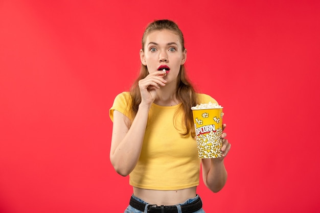 明るい赤の壁の映画館でポップコーンパッケージを保持している映画館で若い女性の正面図