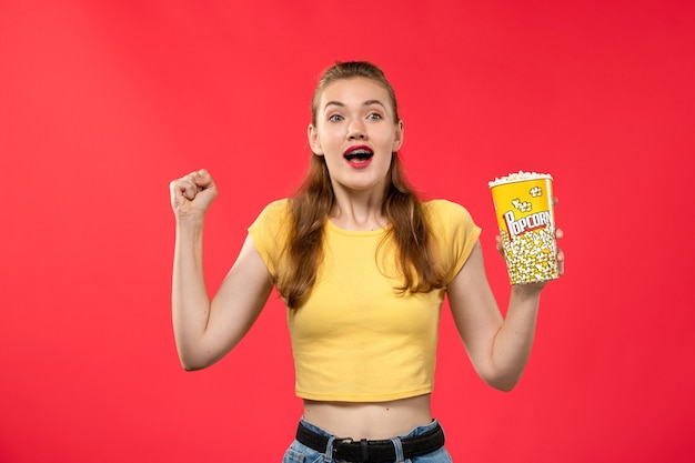 Front view young female at cinema holding popcorn package and rejoicing on red wall movies theater cinema female fun film