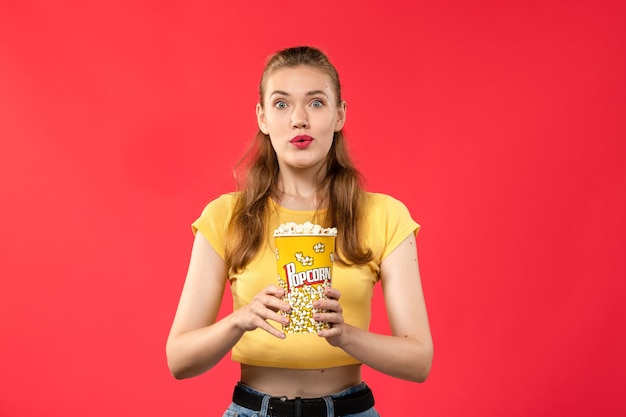 Free photo front view young female at cinema holding popcorn package with excited expression on red wall movies theater cinema film