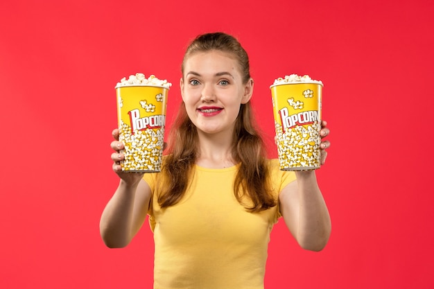 Front view young female at cinema holding popcorn packages on light-red wall movie theater cinema female fun film