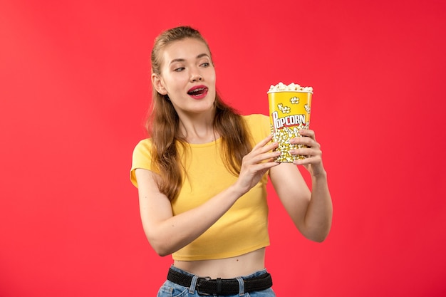 Front view young female at cinema holding popcorn on red wall movie theater cinema female color