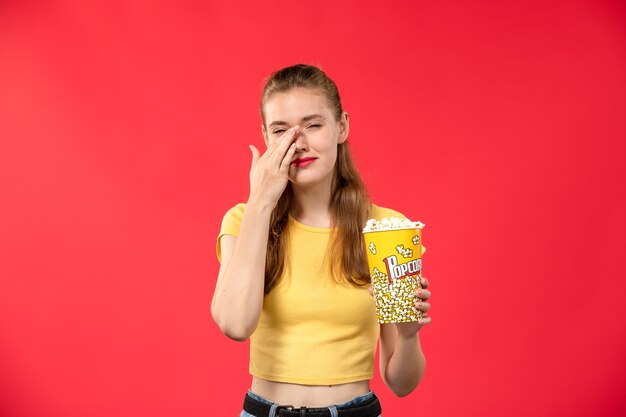 赤い壁の映画館の映画館の女性の色でポップコーンを保持している映画館で若い女性の正面図