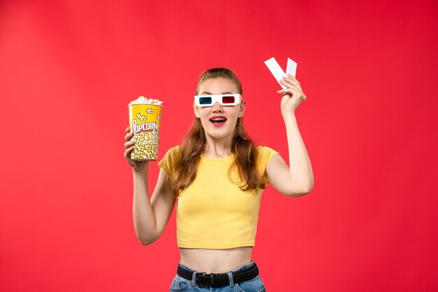 Front view young female at cinema holding popcorn and tickets on the red wall movie theater cinema female colors