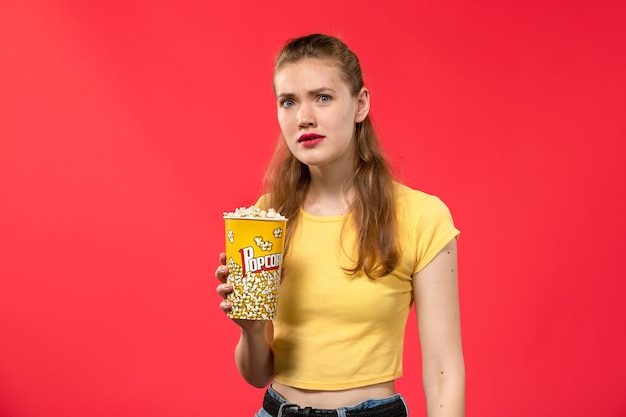 赤い壁の映画館で混乱した表情でポップコーンを保持している映画館で若い女性の正面図映画館スナック女性の楽しい映画