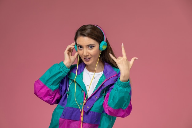 Front view young female in colorful coat listening to music on light pink wall, model woman pose