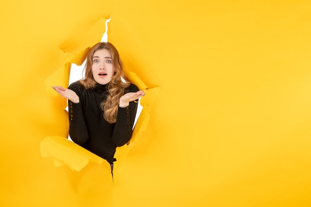 Front view young female confused on yellow ripped wall