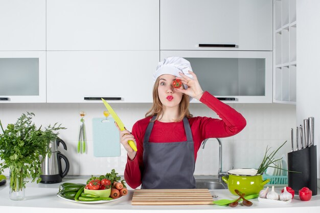 彼女の目の前でトマトを持ち上げてエプロンで若い女性料理人の正面図