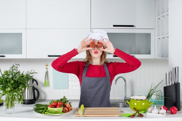 Front view young female cook in apron holding up tomatoes in front of her eyes