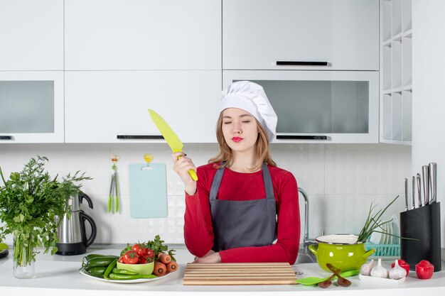 Front view young female cook in apron holding yellow knife