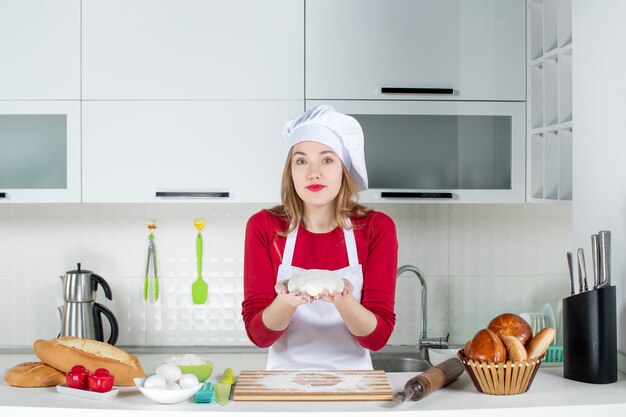 Front view young female cook holding dough in the kitchen