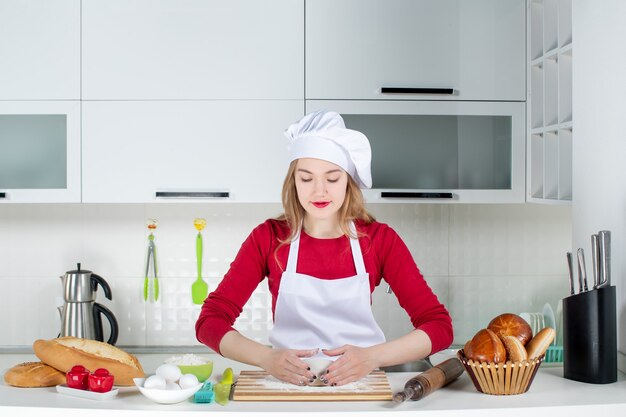 Front view young female cook kneading dough on cutting board in the kitchen